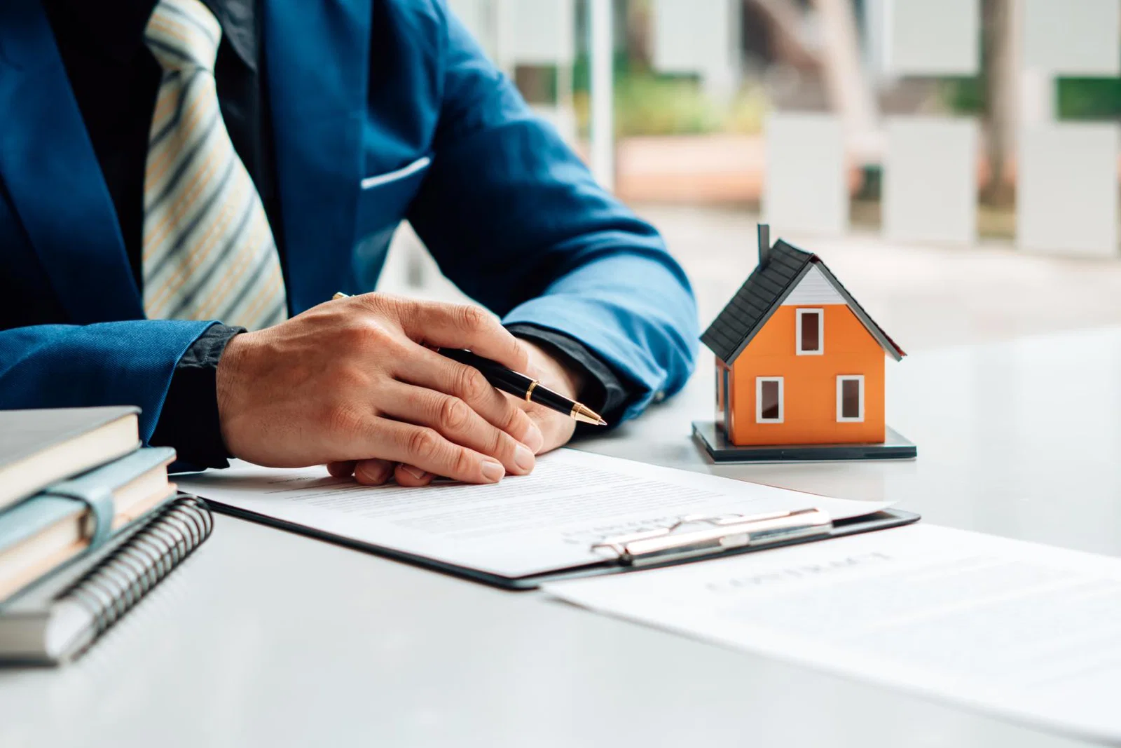 A person sorting their tax affairs at a desk with files, pen and a small model house