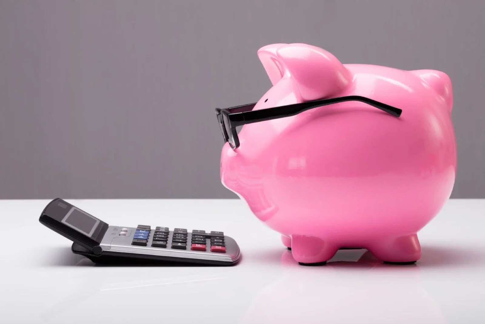 A biggybank pig wearing spectacles looking at a calculator