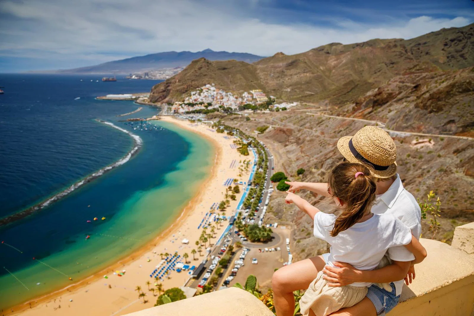 Mother and child sitting on a cliff and looking out over a beach in Tenerife