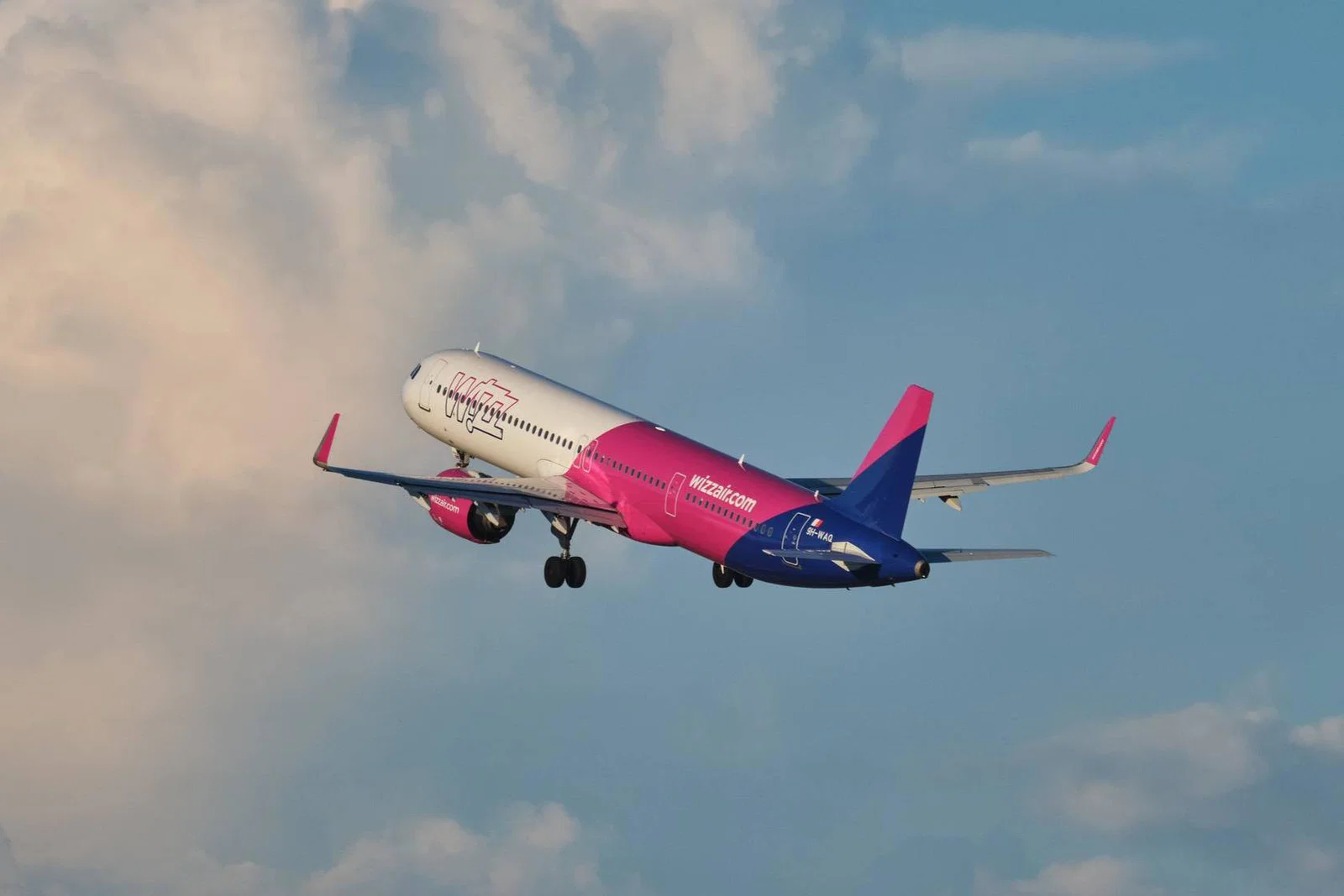 Wizz Air plane mid-flight against a slightly cloudy backdrop
