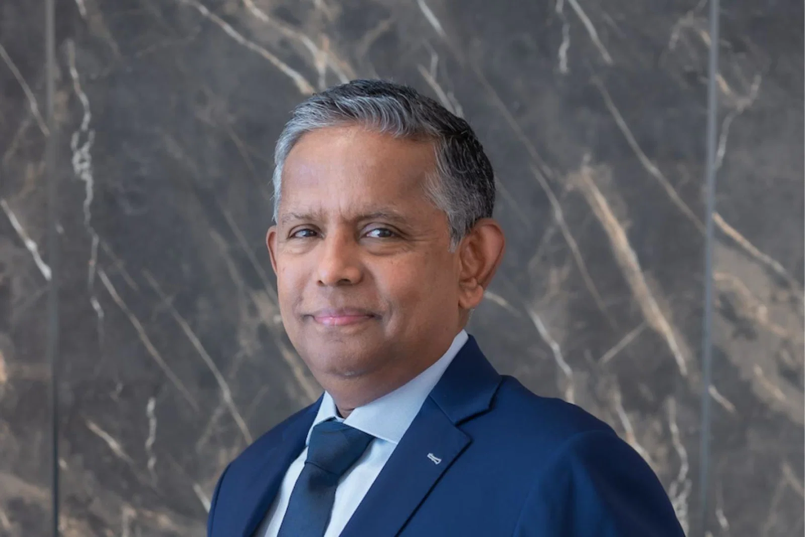 Grey-haired man with light brown skin smiling in blue suit