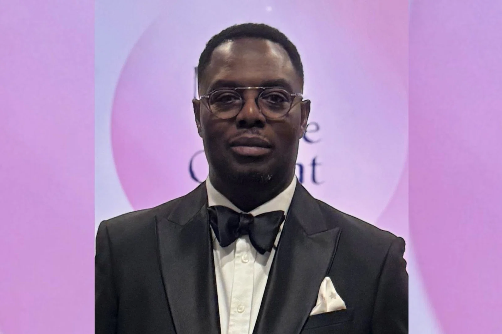 Black man wearing tuxedo, soft pink background 