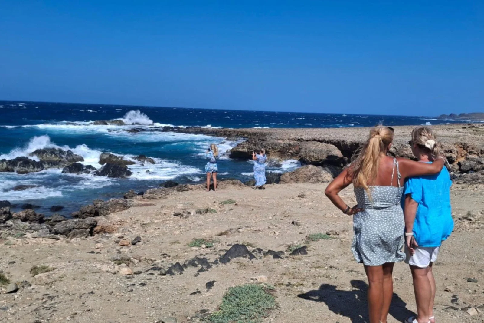 Two blonde women facing rugged coastline 