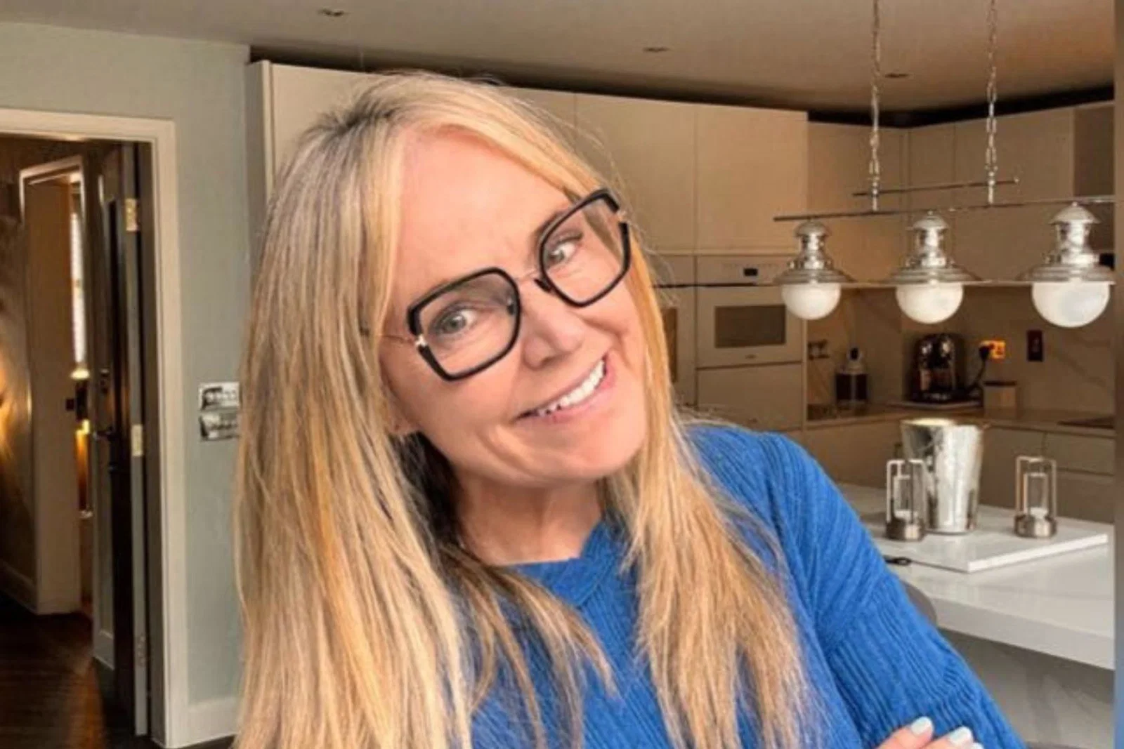 Woman smiling with blonde hair and glasses, her background is a modern kitchen