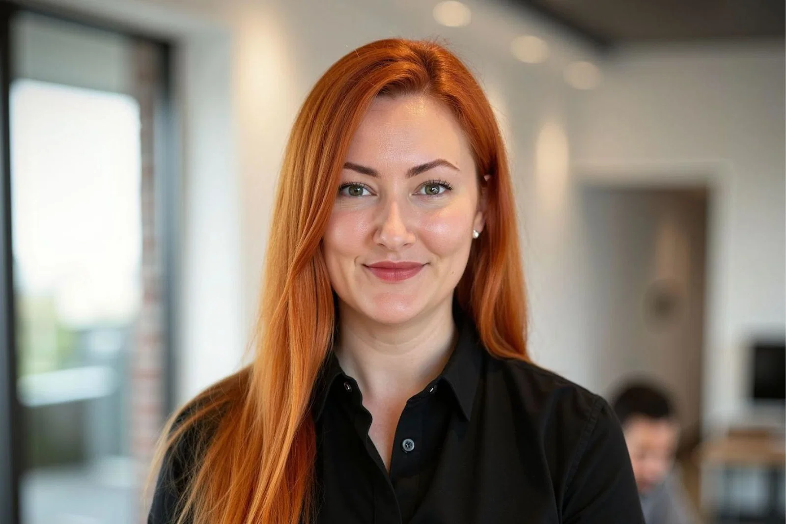 White woman with long, straight red hair and black shirt smiling at camera