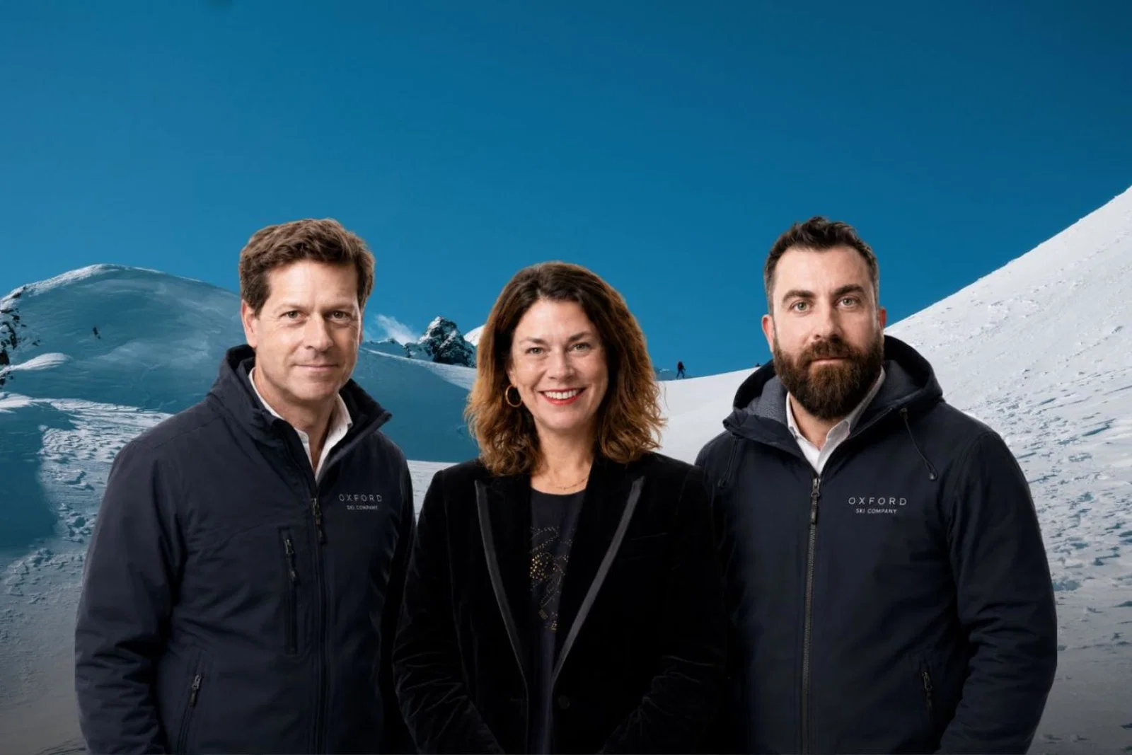 A professional image of a white smiling woman standing with two white men on each side of her, background is snowy ski slopes 