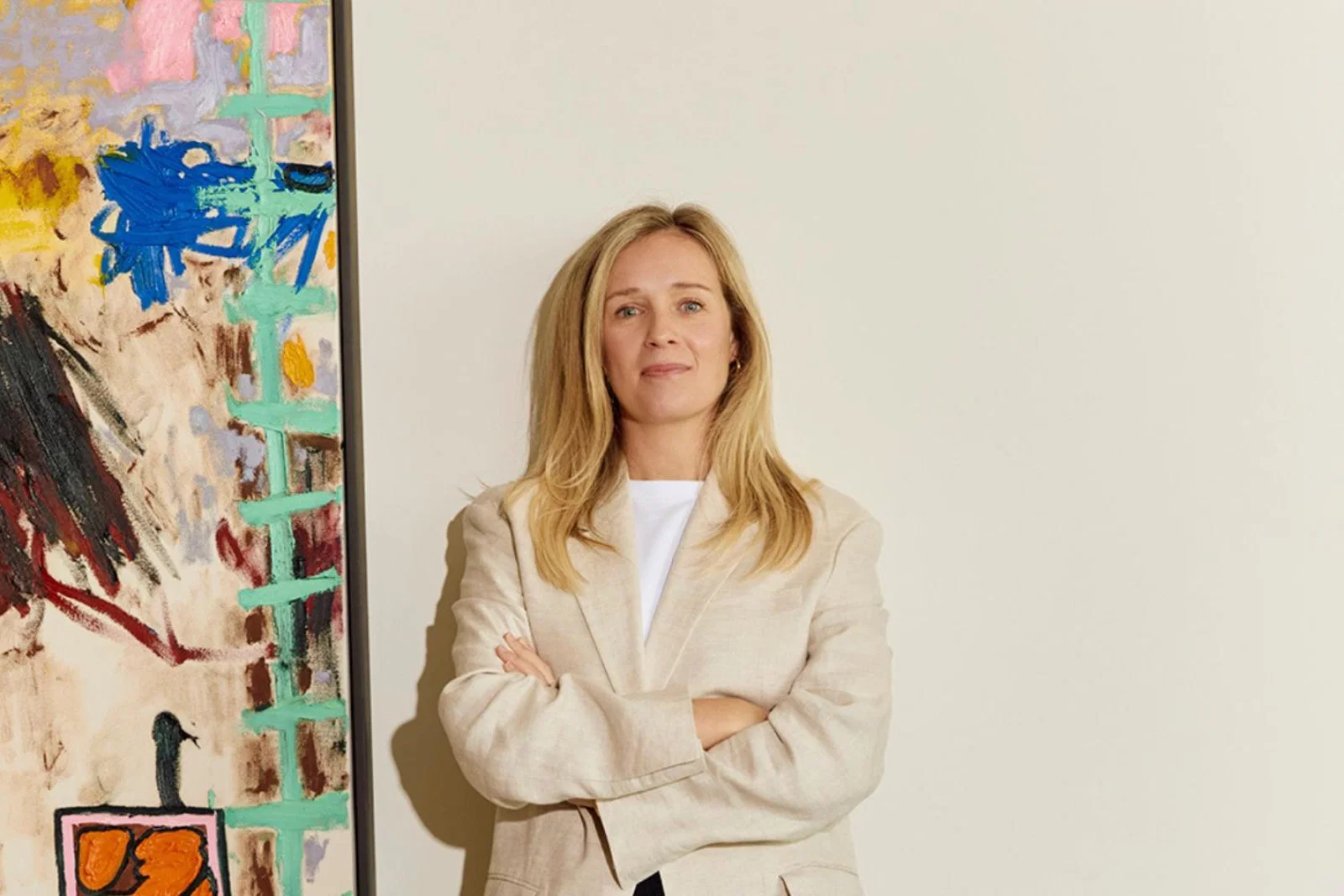 Blonde woman standing in front of white wall, to the left is a painting 