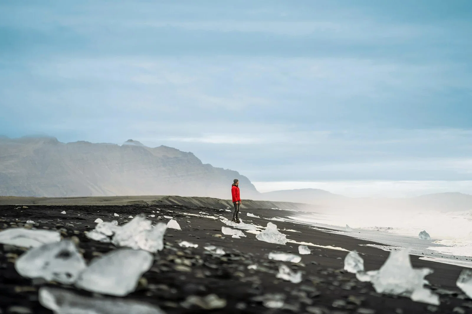 A solo traveller looks out to sea from an Icelandic beach scattered with ice