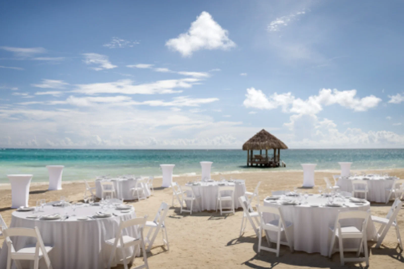 Wedding tables and chairs set up on a white sand beach overlooking the ocean.