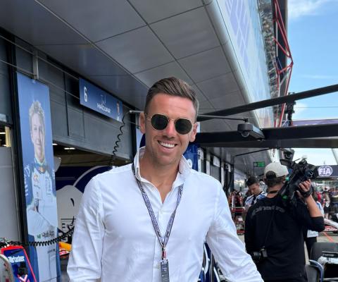 Smiling man wearing sunglasses and white shirt, F1 background 