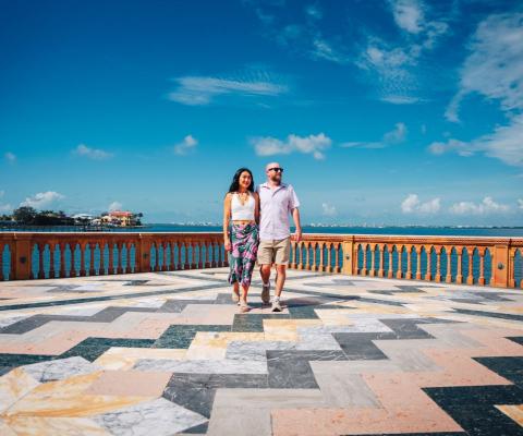Couple stand in the middle of large mosaic floor with blue sky above
