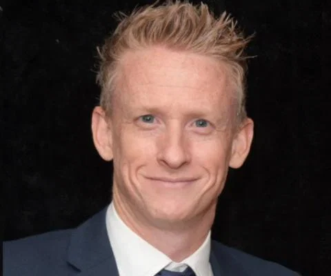 Head shot of white middle-aged man with short blonde hair smiling and wearing suti 