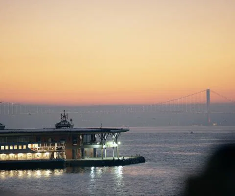Istanbul’s waterfront and illuminated Bosphorus Bridge at sunset, with a ferry docked in the foreground.