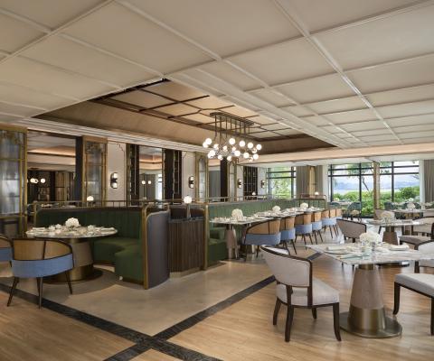 Elegant dining room at Yulong Mansion with green velvet booths, marble tables, and brass accents, with windows overlooking Ha Long Bay.