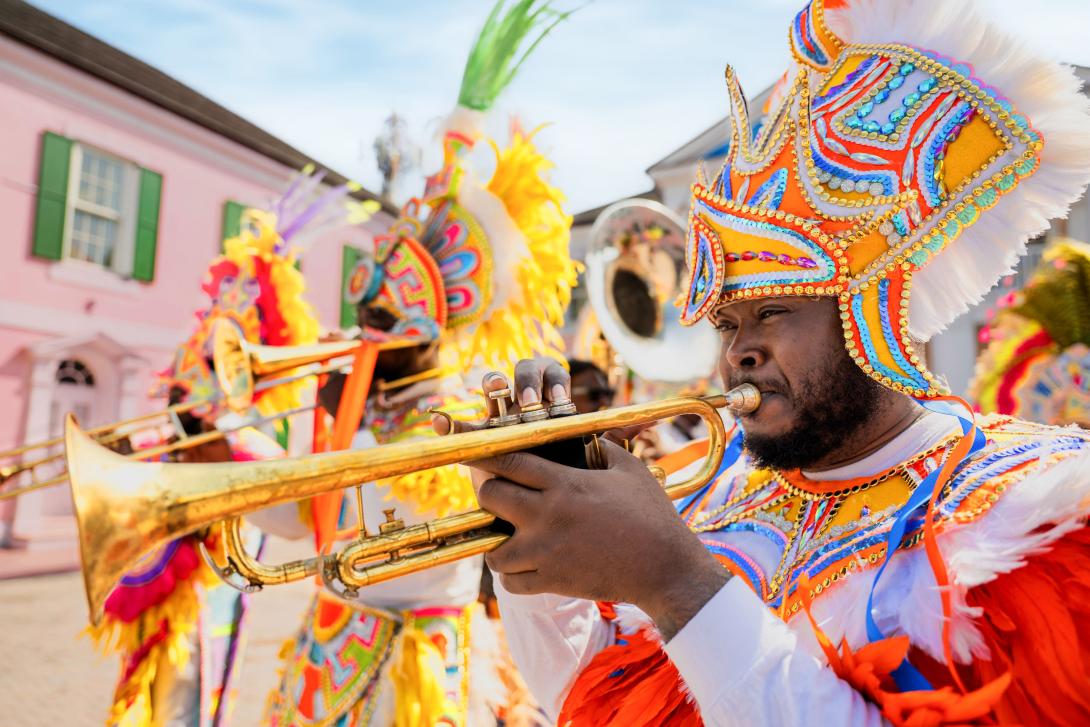Three people wearing colourful feather headdresses playing trumpets