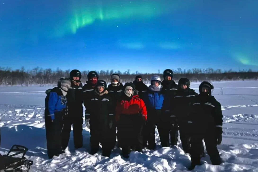 Group of people standing in snow with Northern Lights behind them