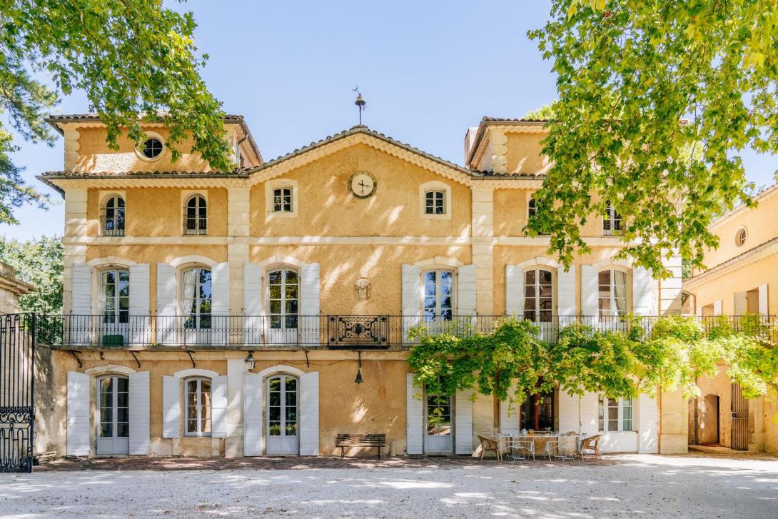 A large, three storey yellow chateau in France with white shutters and a clock on the wall