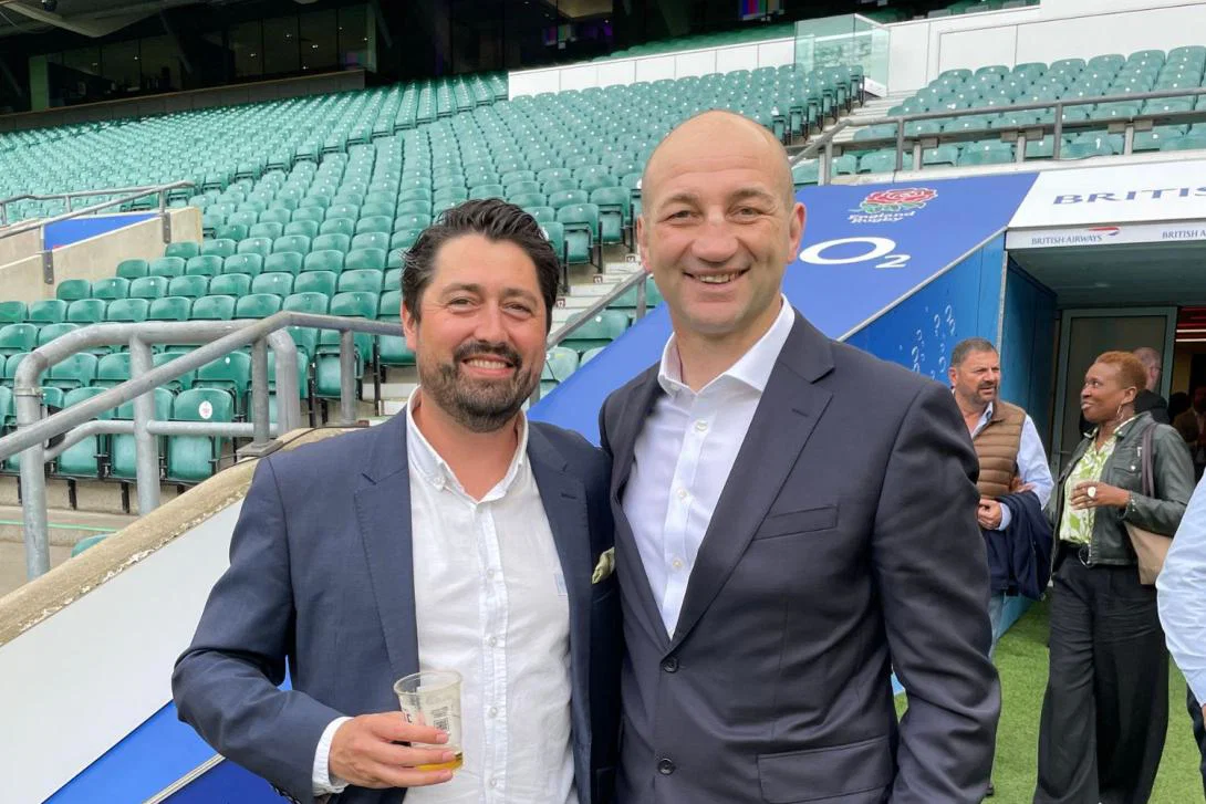 Two white men smiling in suits at a sporting game