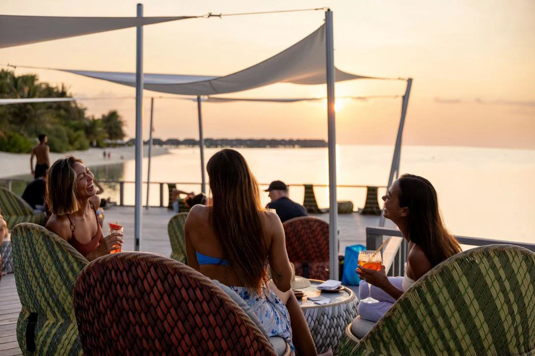 Women having drinks outside by the sea at sunset