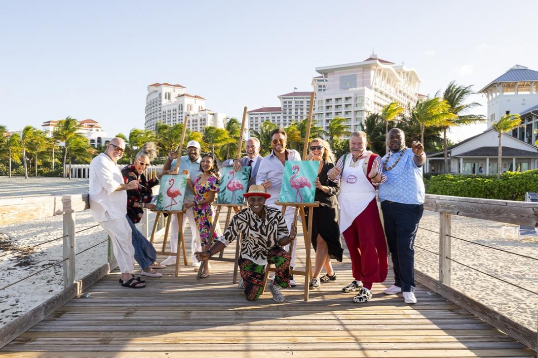 NPIPB Group of people standing on a boardwalk over the ocean with paintings of art next to them and hotel in background