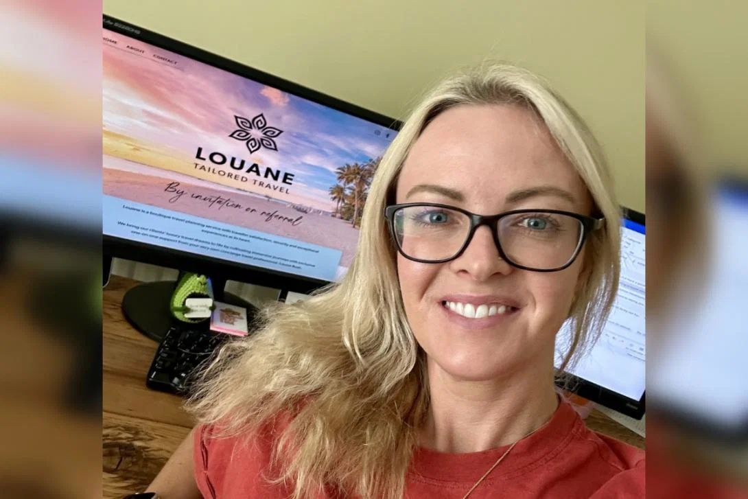 Blonde woman with glasses smiling in front of computer screen
