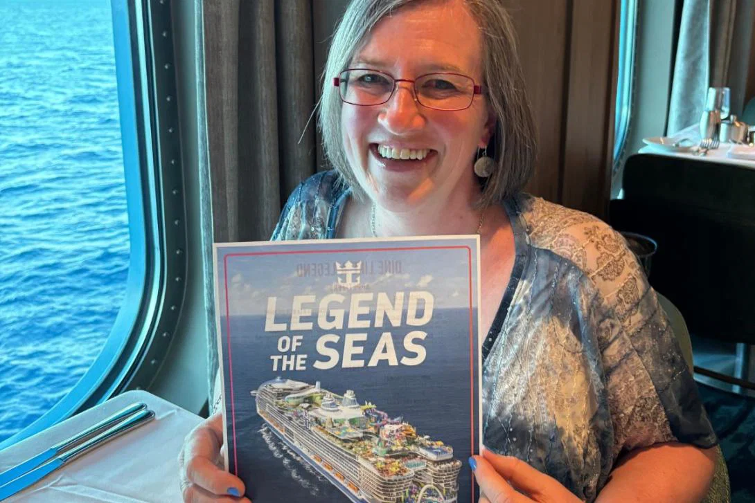 Lucy McRae Lucy McRae sitting at a dinner table holding up a poster for the Legend of the Seas ship