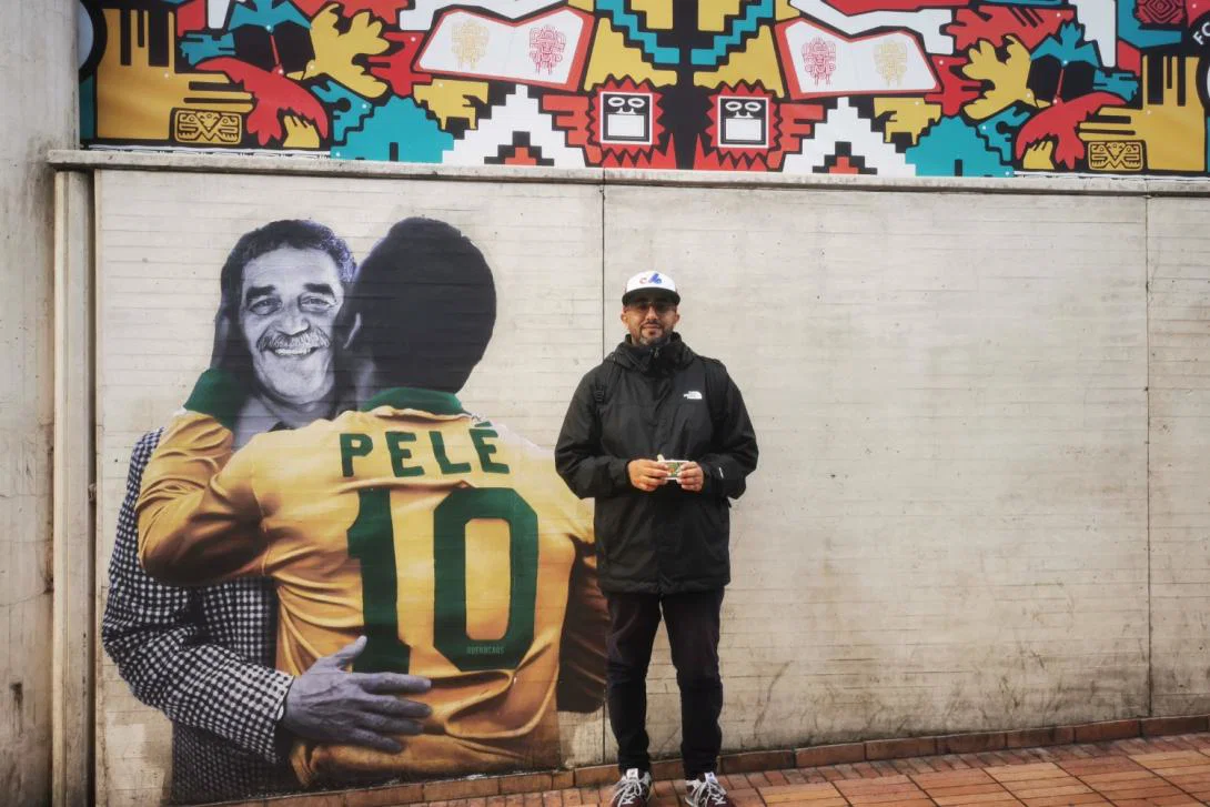 Smiling young man standing beside a mural of Pele in Colombia